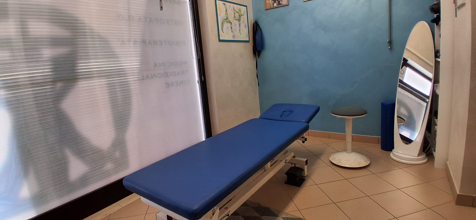 Sala di esame chiropratico con lettino color bordeaux e modello di colonna vertebrale.